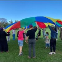 Several adults and children are holding a colorful piece of fabric while playing a fun game