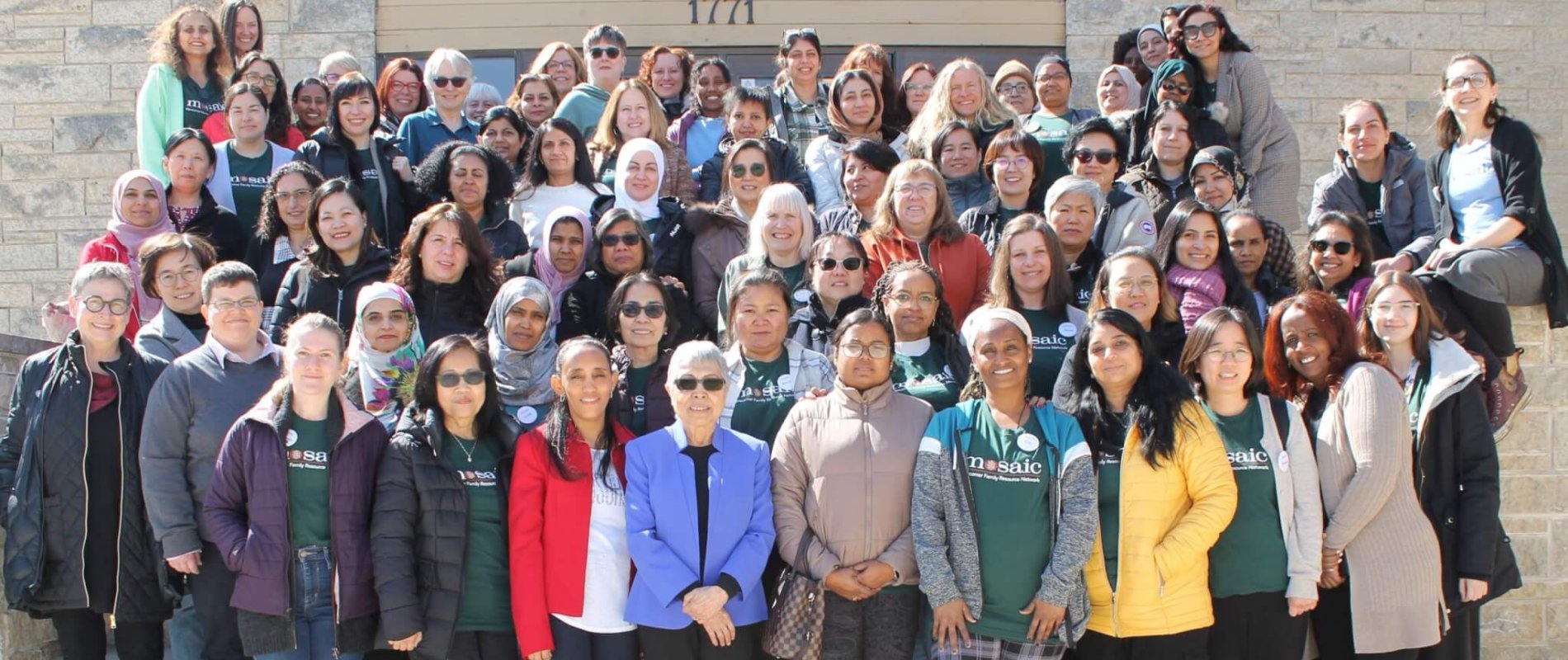 A team of around 60 people in Mosaic shirts, happily smiling on a bright spring day.