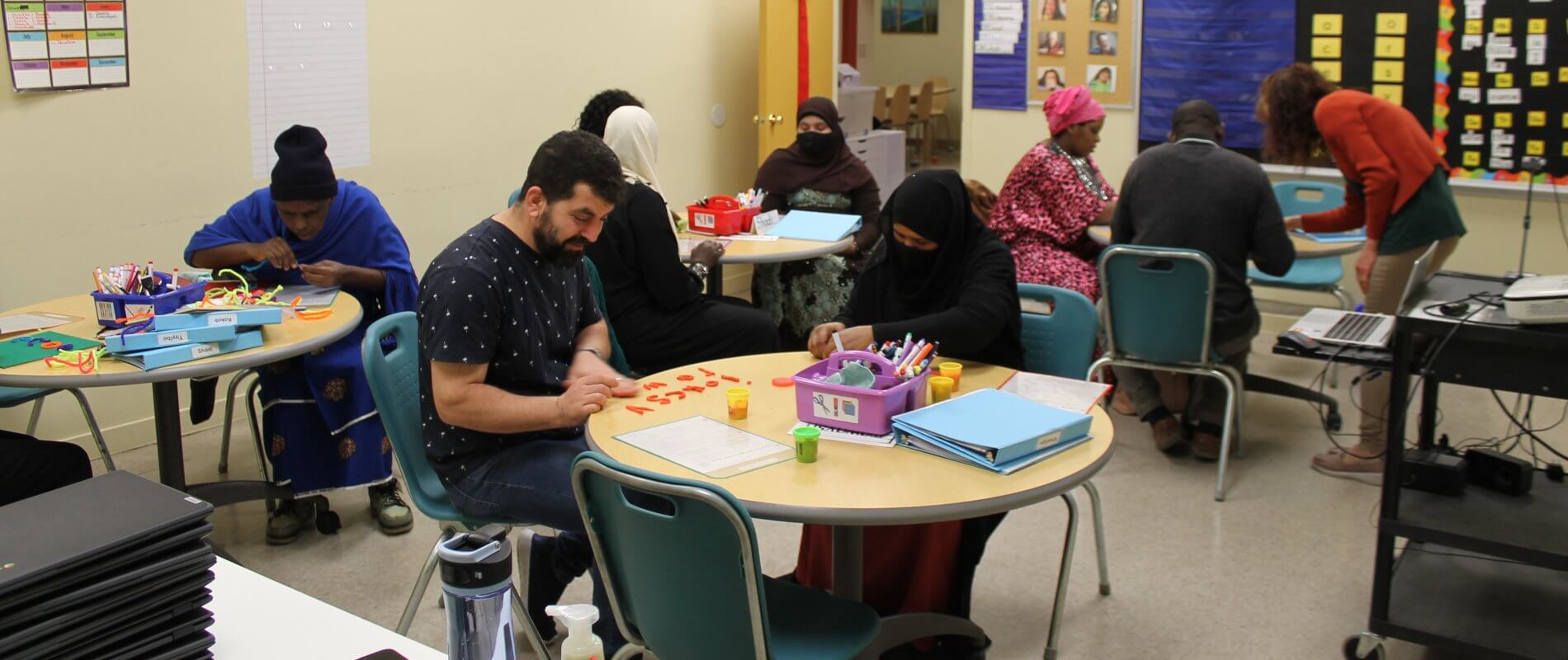 a number of adult students are learning letters in class with teacher's assistance